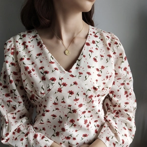 Detail of gold coin pendant necklace worn with a white floral V-neck dress for daily style