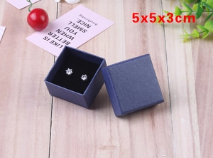 Top view of a 5x5x3cm deep blue textured jewelry box with earrings on wood background