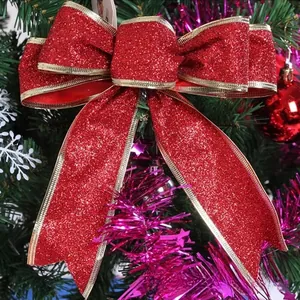 Sparkling red Christmas bow with gold edges hanging on a decorated evergreen tree branch