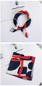 Detailed view of square silk scarf with red and navy geometric patterns on a white desk
