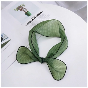 Détail d'un foulard en soie vert olive à pois noué en nœud sur une table blanche