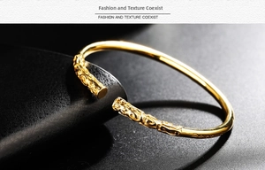 Macro detail of golden open cuff bracelet with intricate carved cloud patterns on the tips