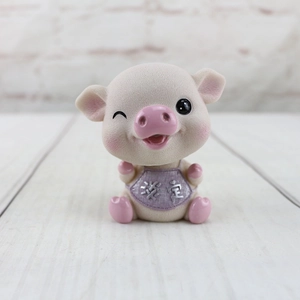 Détail d'une figurine de cochon rose en résine avec un bavoir violet et texte