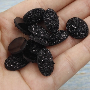 Close-up of 13x18mm oval resin rhinestones with glitter texture held in hand
