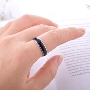 Minimalist silver-edged ring with black enamel center worn on finger with book background