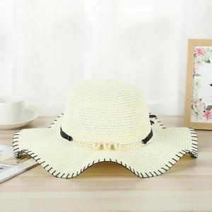 Detail of beige straw sun hat with pearl chain decoration and elegant wavy edges