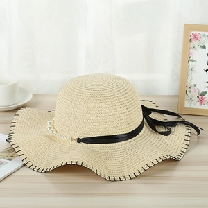 Detail of elegant straw hat with black ribbon bow and white pearls on wooden surface