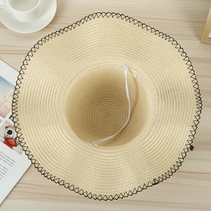 Close-up of woven straw hat with black zigzag stitching and white elastic wind strap