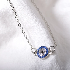 Macro detail of silver evil eye anklet with blue and clear crystals on white linen