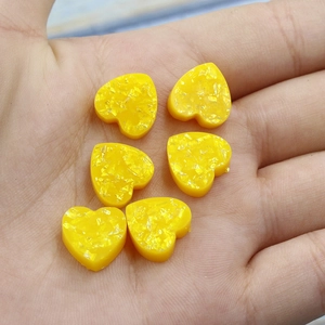 Six yellow heart-shaped synthetic opal resin charms held in palm for size scale