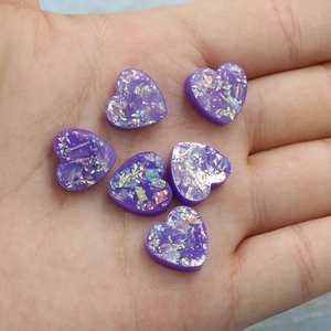 Close-up of six purple heart resin charms with holographic glitter for DIY jewelry crafts