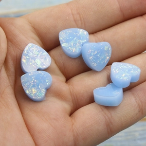 Macro shot of 12mm light blue heart-shaped resin opal stones held in palm for DIY