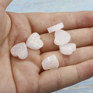 Macro detail of 12mm white resin opal heart charms with glitter finish on palm