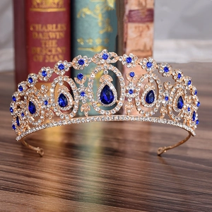 Ornate gold bridal crown with blue teardrop crystals displayed on a wooden surface