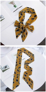 Detail of a ginger yellow silk scarf with geometric patterns tied in a bow on a white stand
