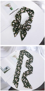 Detail of dark green floral silk scarf tied in a bow and laid flat on a desk