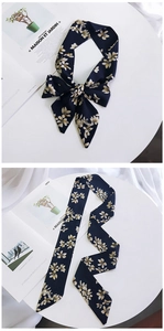 Detail of navy blue floral silk scarf tied in a bow and laid flat on a stylish desk