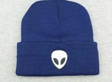 Detail of navy blue knit beanie featuring a white alien head embroidery on the folded cuff
