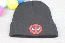 Detail shot of black knitted beanie with red Deadpool mask patch embroidery on flat gray surface