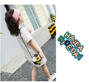 Outdoor shot of a toddler girl wearing a cute bee-shaped crossbody bag with a slim black strap