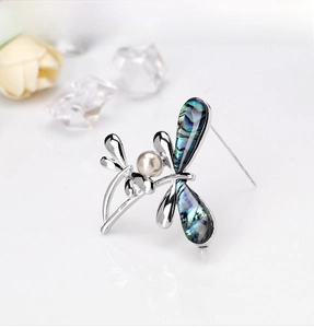 Macro detail of silver dragonfly brooch with iridescent abalone shell wings and pearl