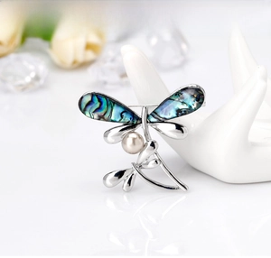Detail showing dragonfly brooch with abalone shell wings and white pearl on a display