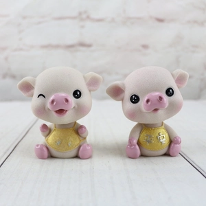 Gros plan de deux figurines de cochons en résine avec bavoirs dorés et caractères porte-bonheur