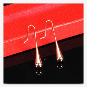 Macro shot of rose gold teardrop earrings hanging on a luxury red textured jewelry box