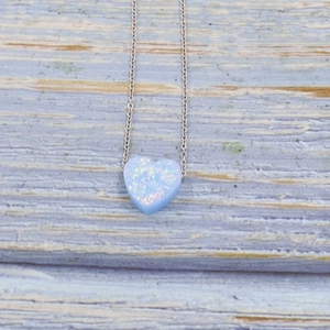 Minimalist silver necklace with heart-shaped blue opal pendant on a rustic wood background