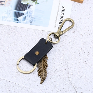 Vintage bronze feather leather keychain with metal carabiner on a marble background