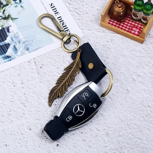 Close-up of vintage bronze feather charm and black leather strap keychain with car key