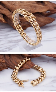 Detail of chunky gold Cuban link bracelet with press buckle on marble and wood background