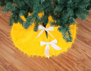 Detail of yellow plush Christmas tree skirt with white bows on wooden floor