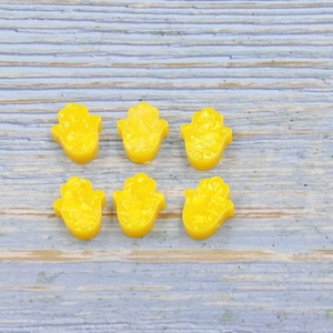 Macro shot of yellow Hamsa Hand resin beads with opal glitter on light wood background