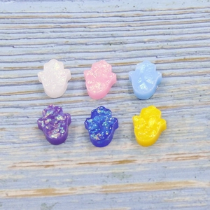 Colorful resin Hamsa Hand beads with glitter effect arranged on blue wood background