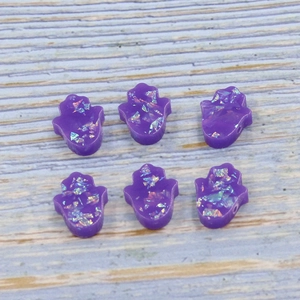 Macro detail of six purple Hamsa hand opal beads with iridescent flakes on wood surface