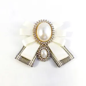 Elegant ivory ribbon bow brooch with pearl and rhinestone accents on white backdrop