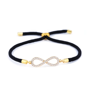 Dettaglio del bracciale infinity dorato con zirconi bianchi su cordino nero intrecciato
