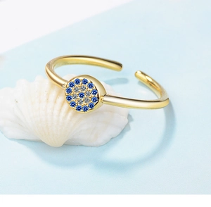 Macro side view of gold evil eye ring with blue and white zircons on a seashell
