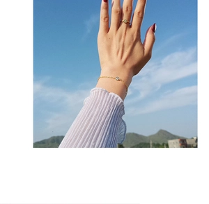Detail of gold evil eye ring and bracelet set worn outdoors against a blue sky