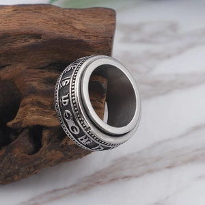 Minimalist stainless steel rotating ring with Tibetan mantra on textured marble surface