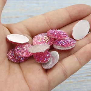 Detail view of 13x18mm pink glitter resin druzy cabochons held by hand for DIY jewelry