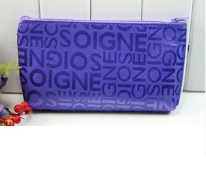 Detail of purple fabric cosmetic bag showing zipper closure and SOIGNE jacquard pattern
