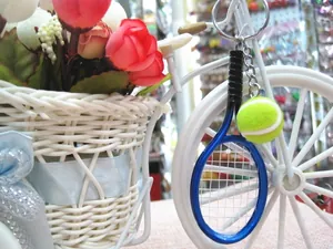 Close-up of blue metal tennis racket and yellow fuzzy ball keychain hanging on decor