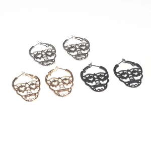 Detailed close-up of hollow skull earrings in gold, silver, and black metal finishes