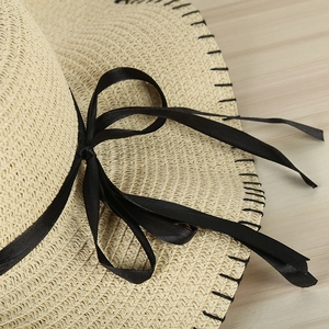 Detailed view of straw sun hat featuring a black ribbon bow and precise stitching