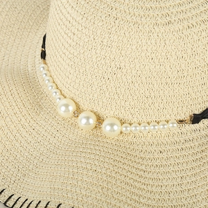 Detailed close-up of woven straw hat featuring elegant pearl band and black contrast stitching