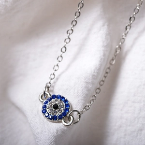 Macro shot of silver evil eye anklet with blue and clear zircon stones on white fabric
