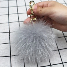 Detail of light gray plush fur pom-pom keychain with premium golden metal clasp