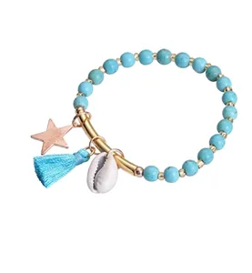Detail of blue beaded bracelet with gold tube, star charm, tassel and seashell accent